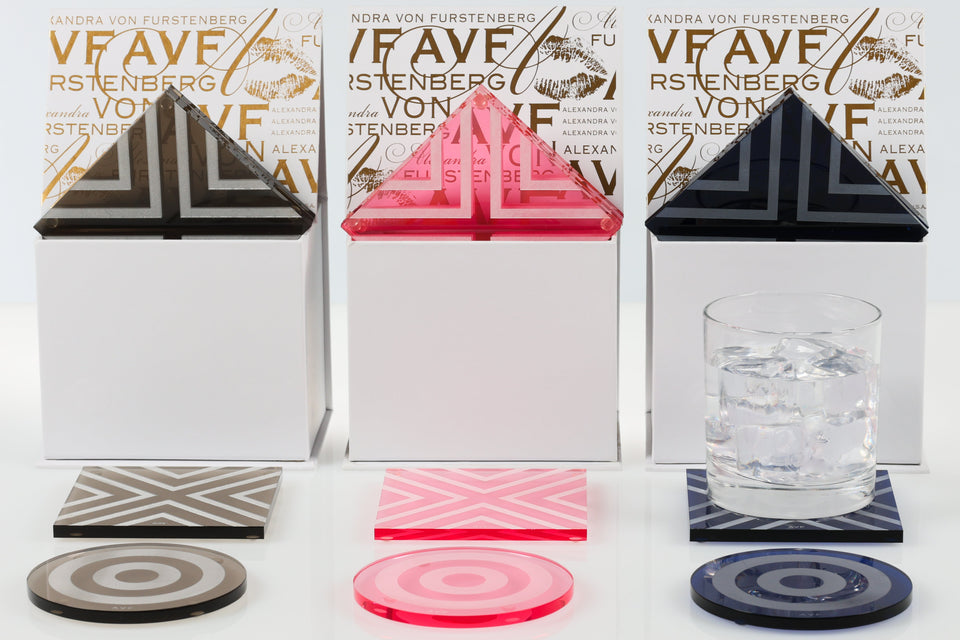 Geometric coasters with triangular and circular designs on a white surface with branded boxes in the background.