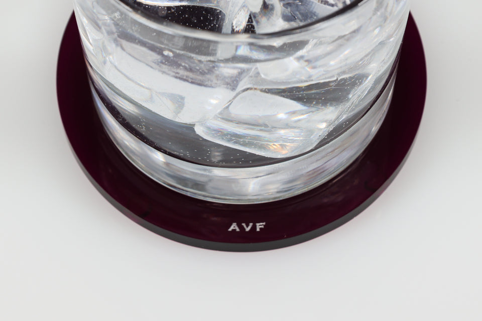 Clear glass container with ice on a amethyst coaster, branded 'AVF'.