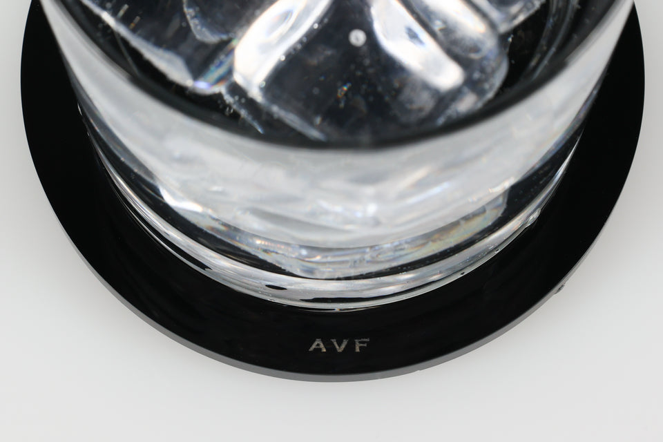 Clear water glass on a black coaster with 'AVF' logo as the focus. set on a white background