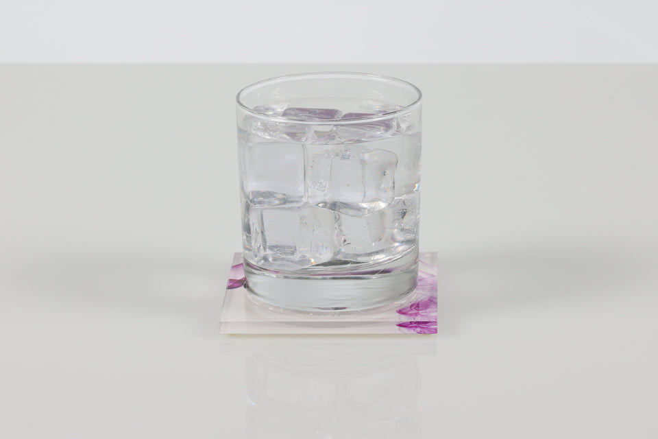 Clear glass with water and ice on a magenta smoke print lucite square alexandra von furstenberg acrylic coaster. 