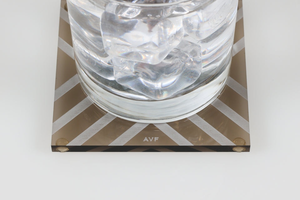 Water glass on bronze AVF chevron coster. zoomed in on the AVF logo