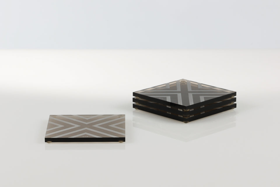 bronze square coasters sitting on a white table. There is a white pattern on the coaster to prevent slipping. One stack of three and a solo next to it. 