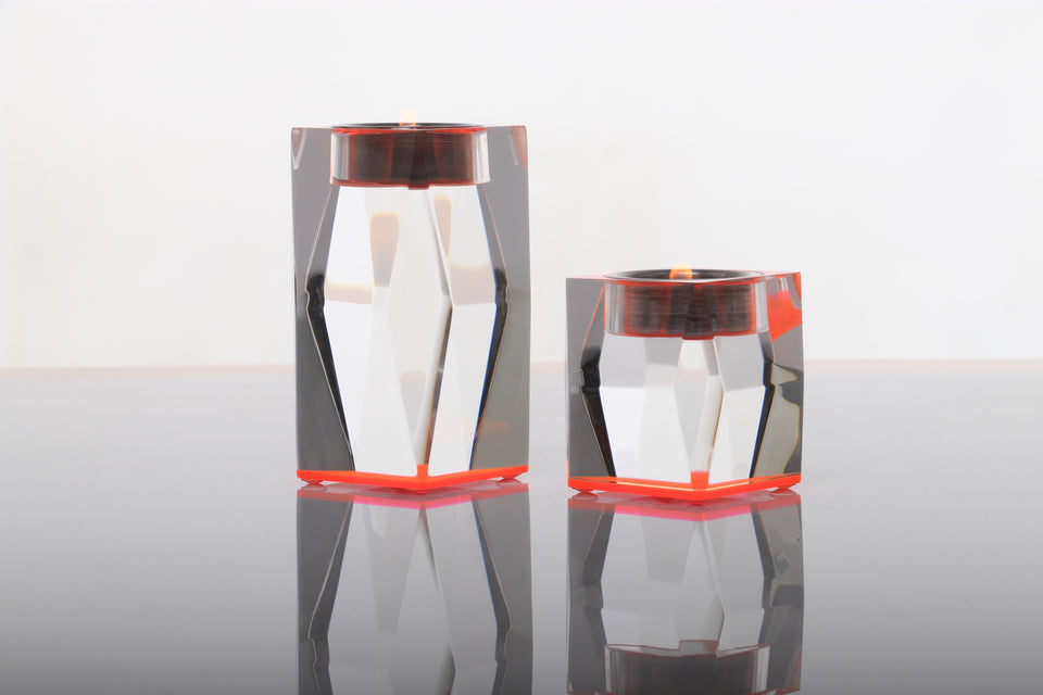 Pair of pink votive candleholders one is short and one is tall. both hold candles which are lit. The candle holders are clear acrylic with a pink base giving the pieces color. 