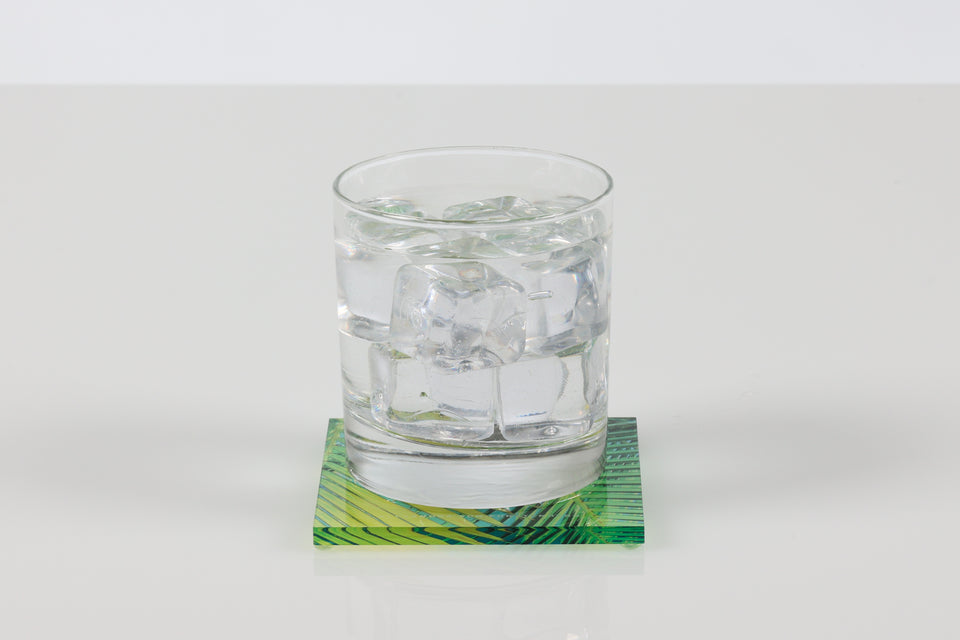 Glass of ice water on a green and yellow palm print coaster. 