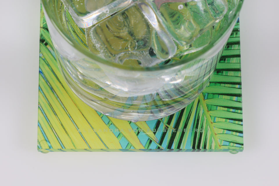 Water glass sitting on a square palm print coaster, focused on the Alexandra Von Furstenberg logo. 
