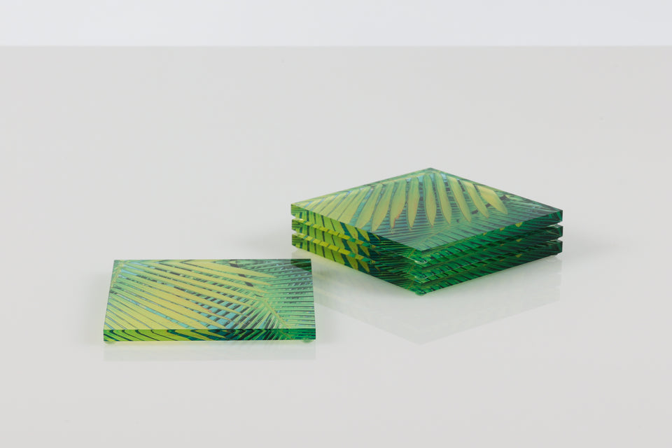 Green and yellow square palm print coasters on a white table. 