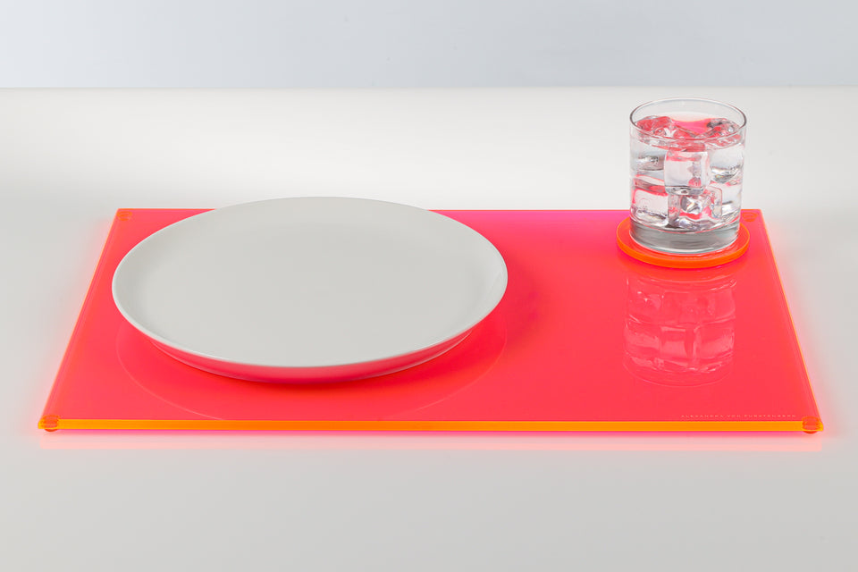 Neon pink placemat with a white plate and glass on a light gray background