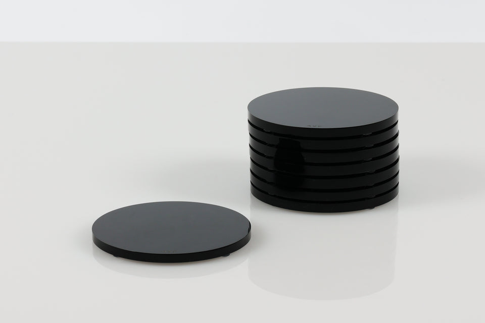 set of black acrylic coasters seven are stacked next to a solo black round coasters