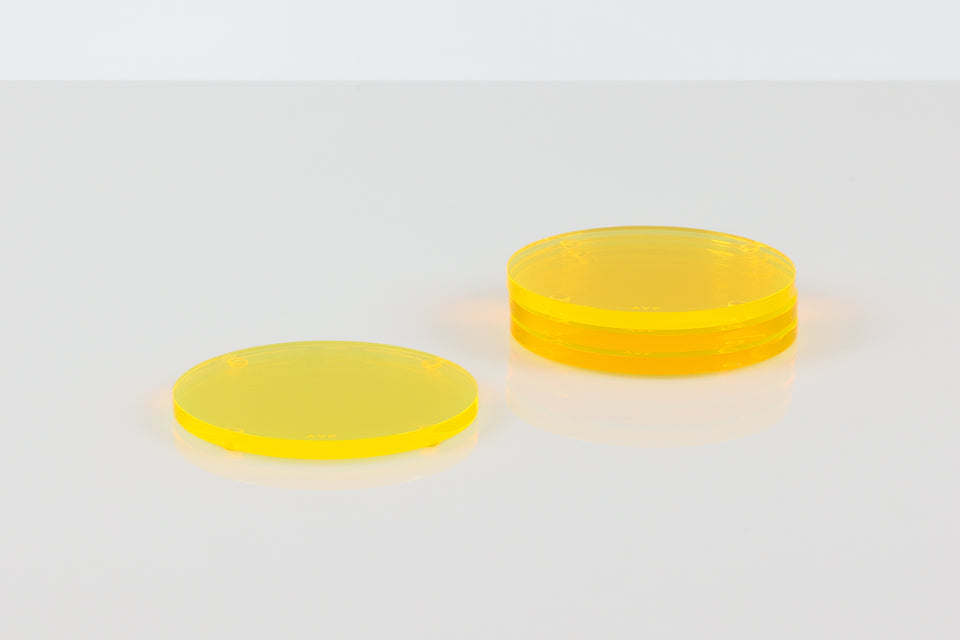 Stack of 3 yellow round lucite AVF coasters set next to a solo coaster. set on a white table. 