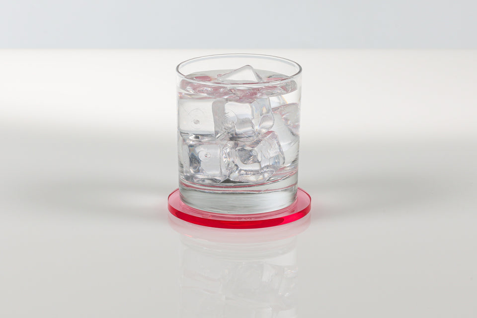 Glass of water with ice cubes on a white background resting on a tulip acrylic coaster. 
