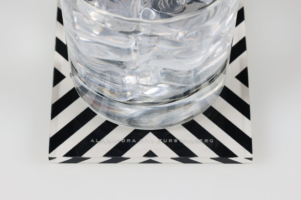Alexandra von Furstenberg X-Print coaster zoomed in on the logo. A glass with water rests on the coaster. 