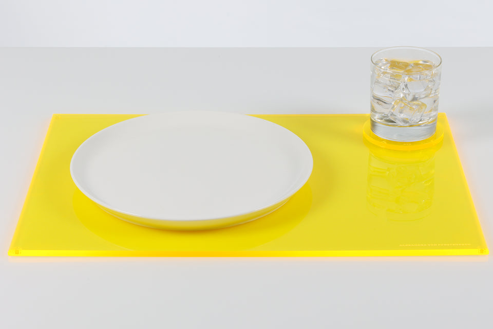 AVF home luxury acrylic rectangle yellow placemat. On the placemat sits a round white plate and a round AVF yellow coaster holding a glass of water. 
