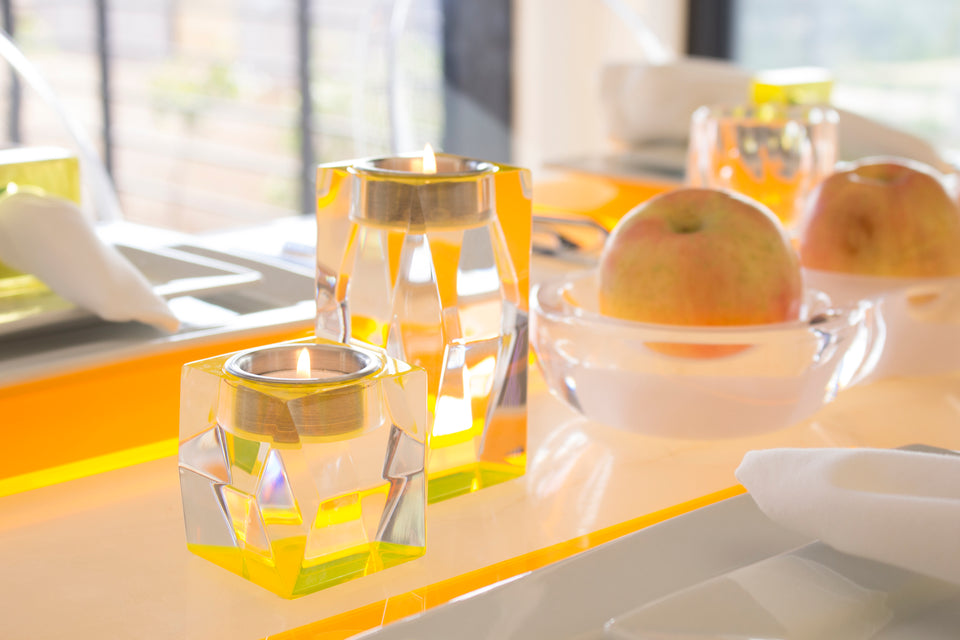 Acrylic yellow accessories mainly focusing on pair of yellow tea light candleholders. Set on a dinner table