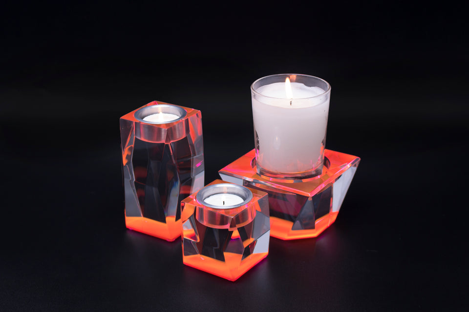 Acrylic pink candleholders. Body of the acrylic candleholders are clear with a pink base bringing out the color. one holder is tall while the others are short. all candles are lit. one candleholder holds a large candle the others only have votives. 