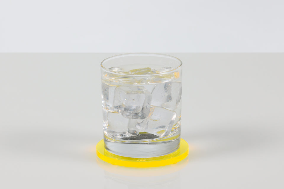 Clear glass with water on a yellow round acrylic coaster against a white background