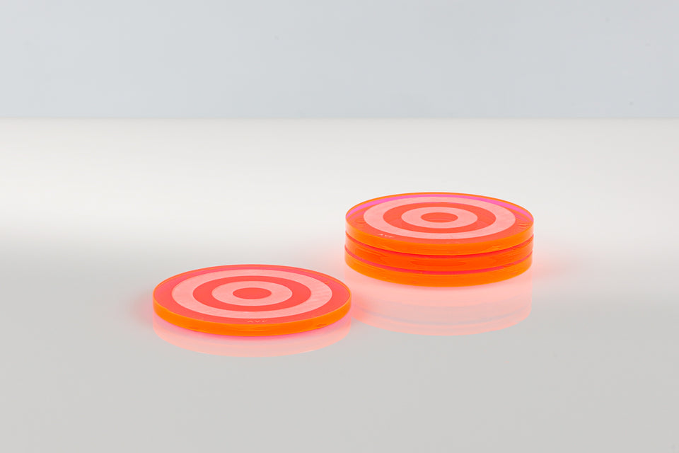 Stack of three next to a solo coaster on a white table. The coasters are pink acrylic luxury coasters with a bullseye design on a white background
