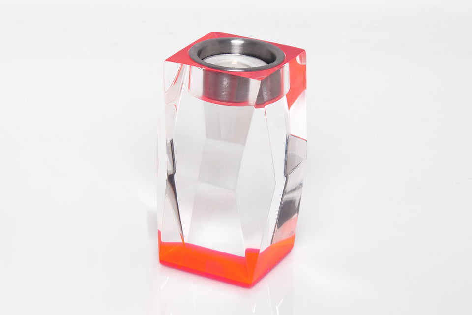 Tall pink candleholder, clear sculpted body with a pink base. Candle is lit in the candleholder. 