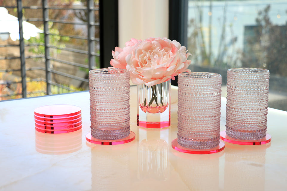Tabletop with acrylic coasters and an lucite vase. Three glasses are sitting on 3 coasters which are on the table in front of the flower vase. 
