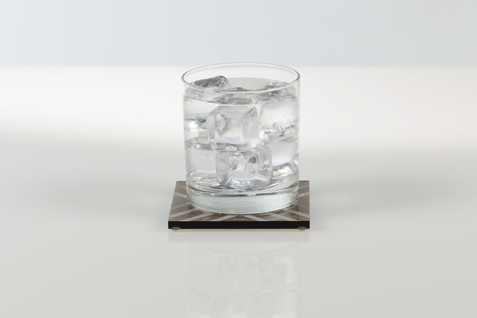 Glass of water with ice cubes on a square bronze AVF coaster. 